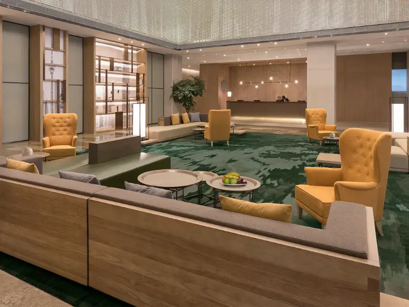 Luxurious hotel lobby lounge with yellow armchairs, modern wood sofas, and green abstract area rug.