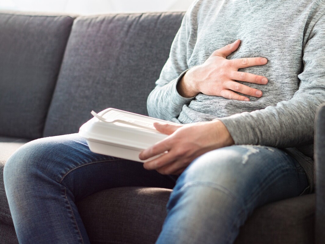 man feeling bloated eating unhealthy food and reducing his calorie deficit after following the best treadmill workouts for weight loss