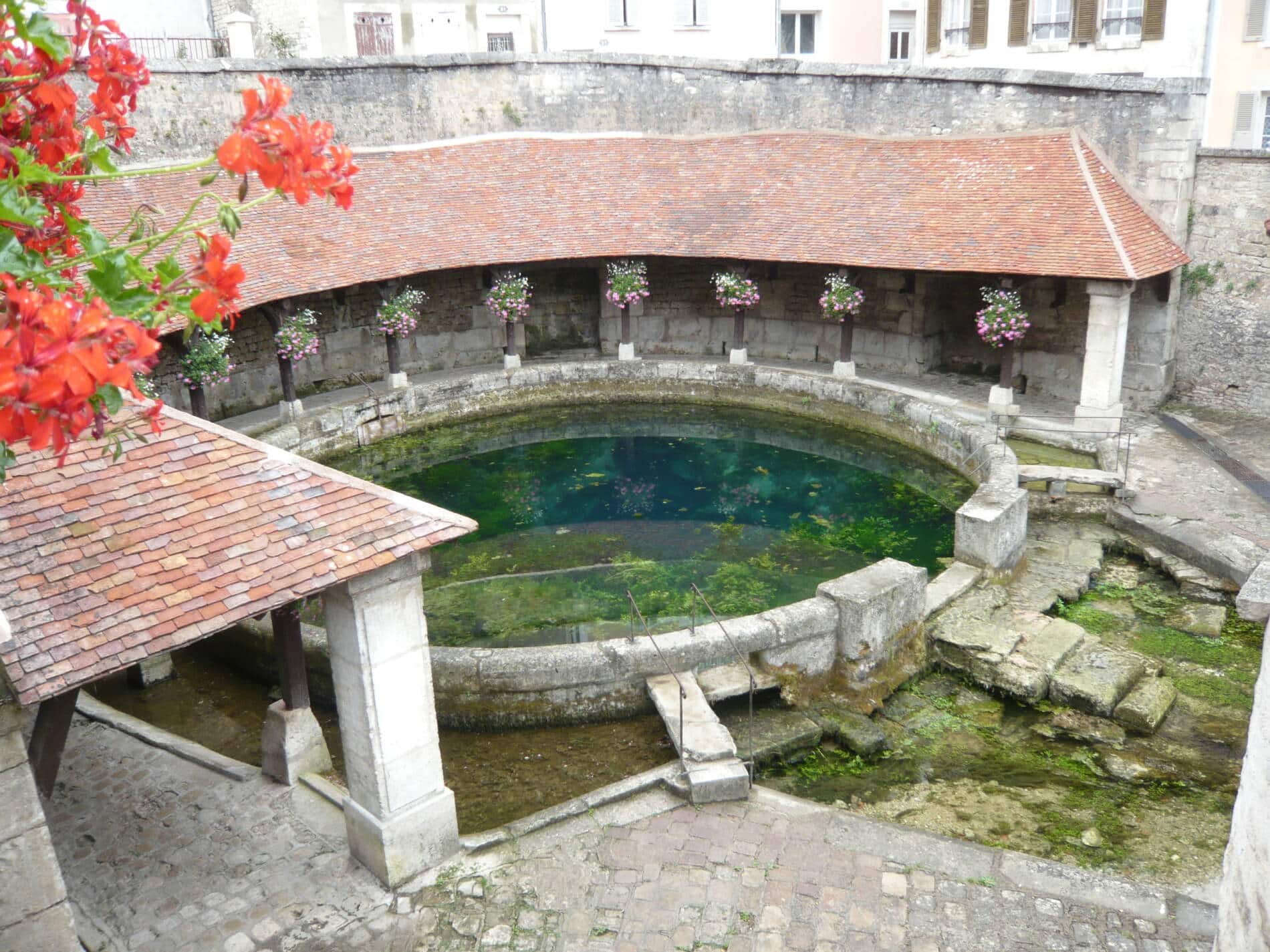 Lavoir circulaire ancien en pierre avec toit rouge et fleurs, Bourgogne-Franche-Comté