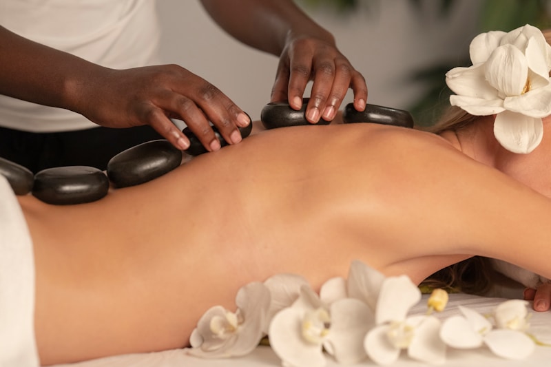 Warm basalt stones placed along a guest's back beside white orchids