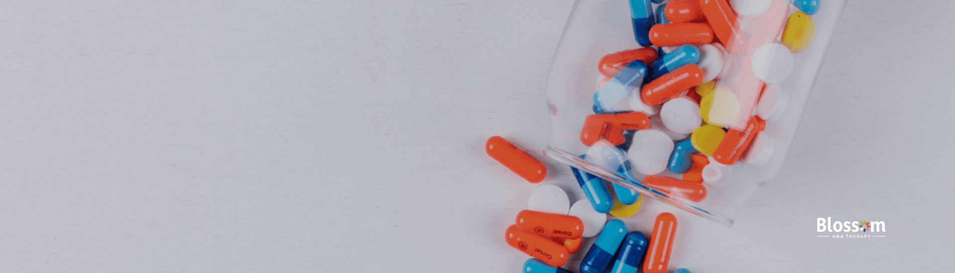 A glass jar tipped over, spilling colorful pills and capsules onto a white surface.