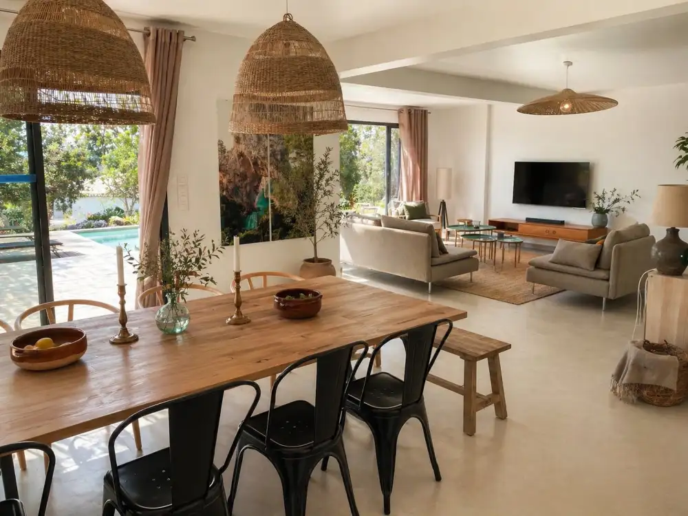 Séjour ouvert d'une maison de vacances en Corse avec grandes suspensions en rotin, table de salle à manger en bois massif et vue sur jardin et piscine