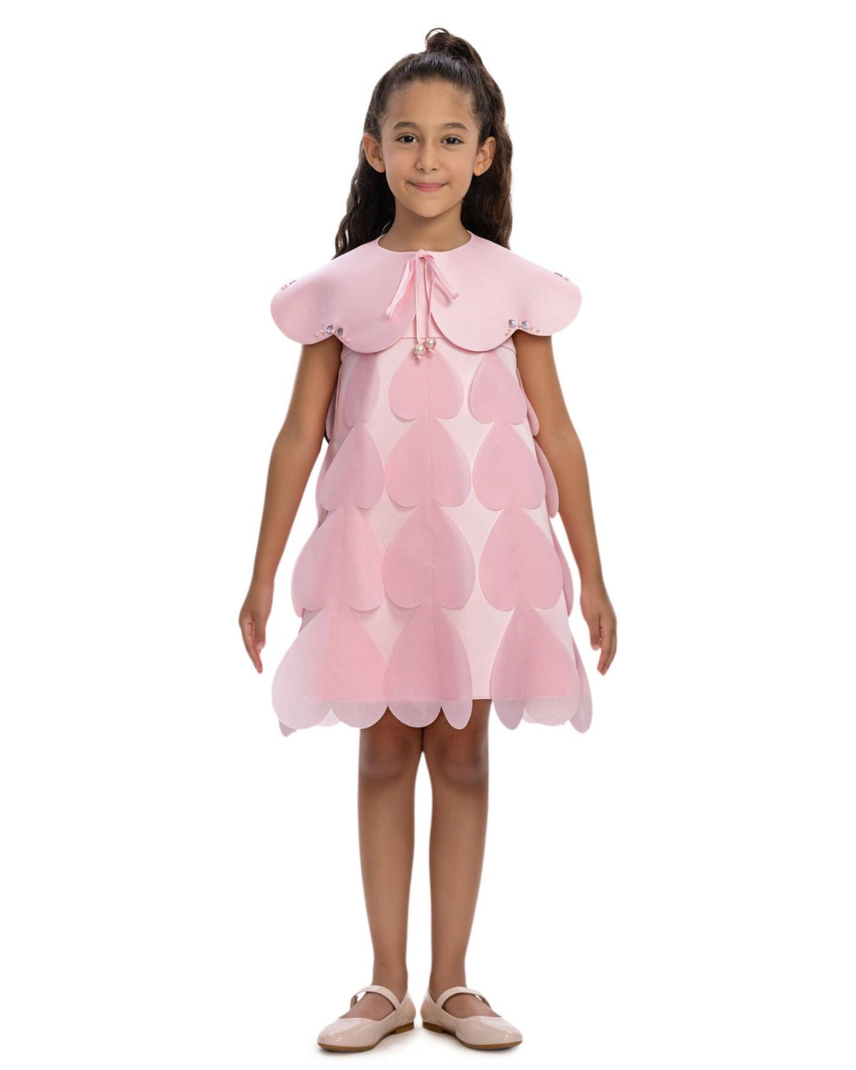 Young girl wearing a pink dress with scalloped edges on a white background