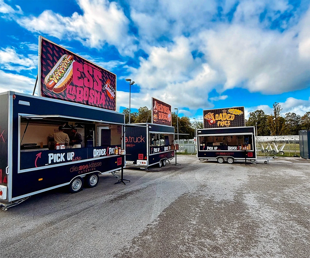A food truck illuminated from within, showcasing a variety of food and drink items against a dark backdrop.