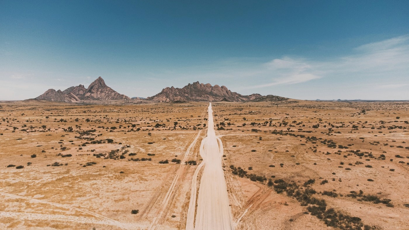 A convoy of 4x4 vehicles driving a Namibian gravel road with dust trailing behind