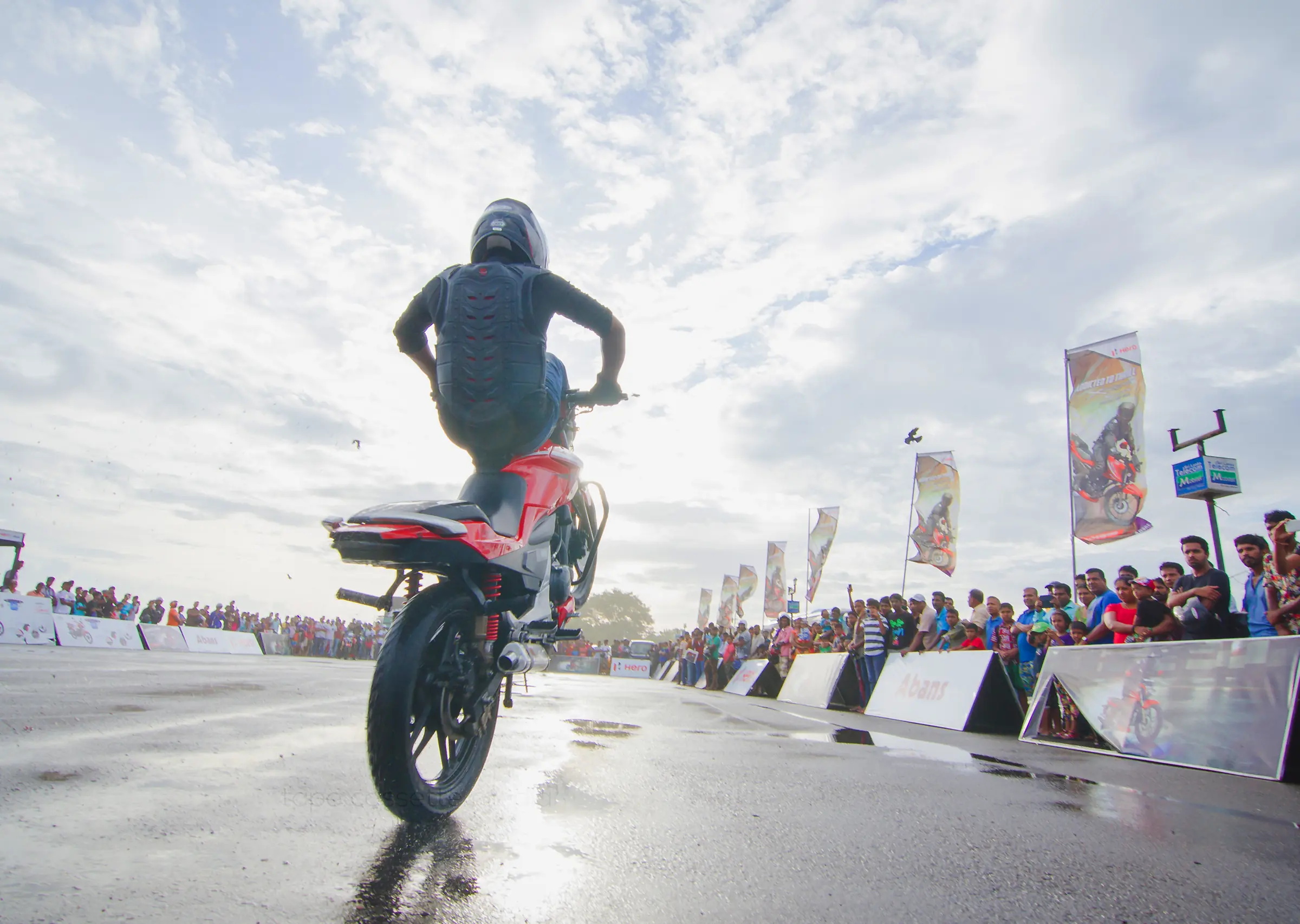 Motorcycle rider performing a stunt outdoors under a clear sky with clouds, wheels grounded in motion