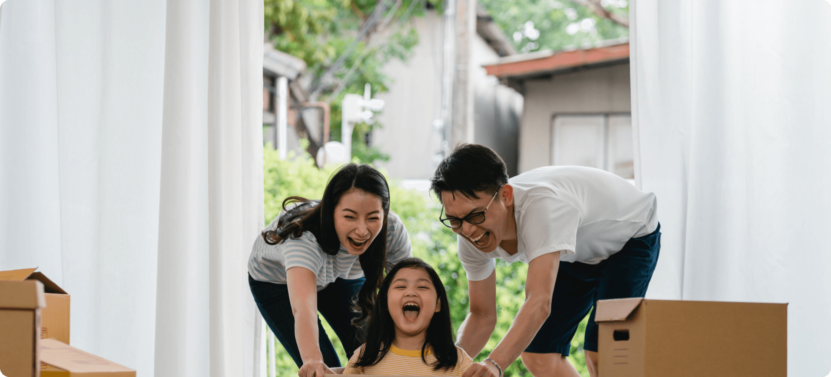 Asian family with young daughter laughing and playing with moving boxes, symbolizing financial freedom and a new home.
