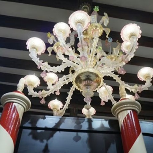 Un lampadario decorativo con dettagli in vetro rosa e bianco sospeso tra due colonne a strisce in un ambiente interno.