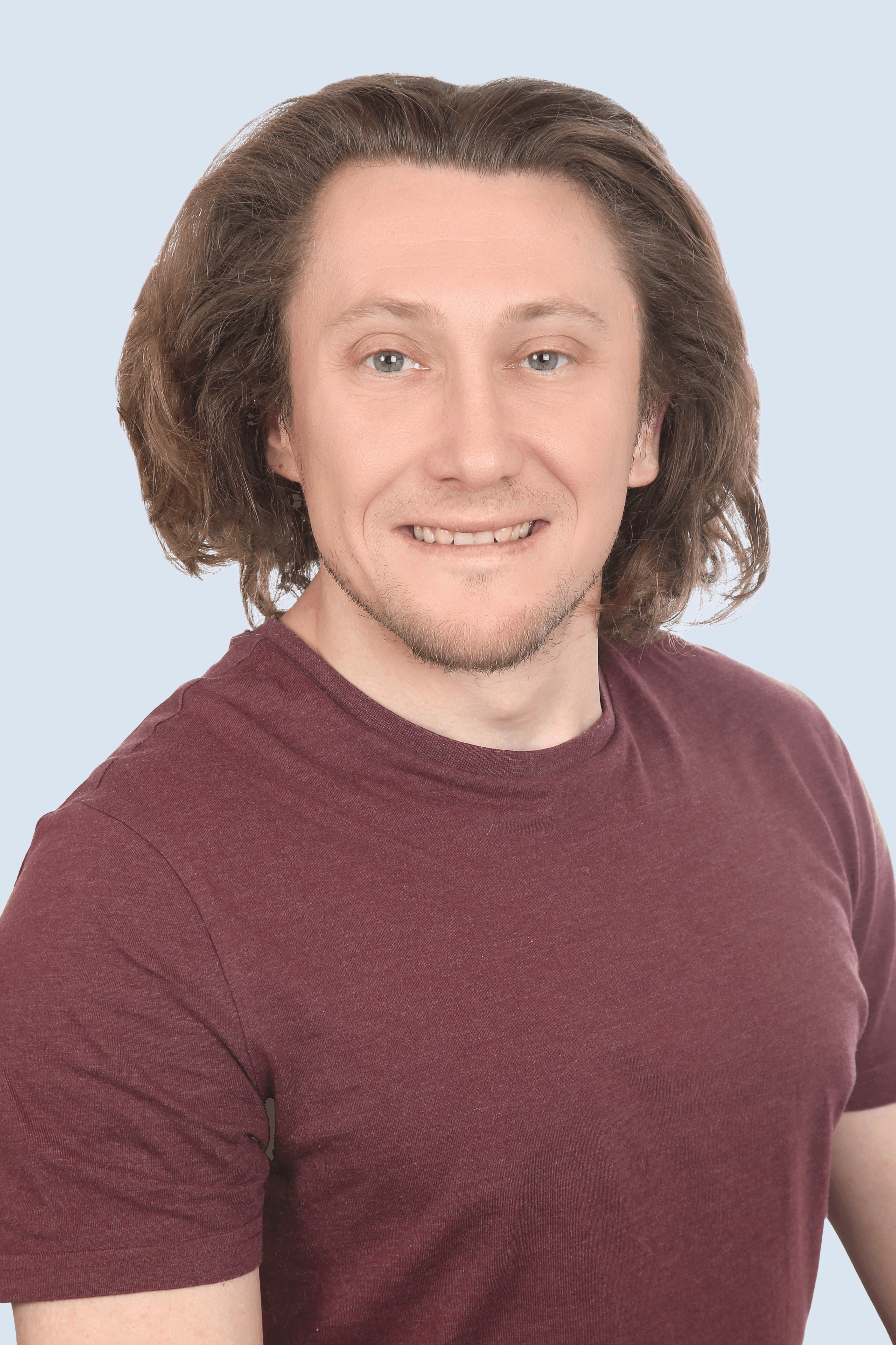 Frau mit braunem Anzug, blauem Hemd und Brille schaut mit verschränkten Armen seitlich in die Kamera und lächelt. 