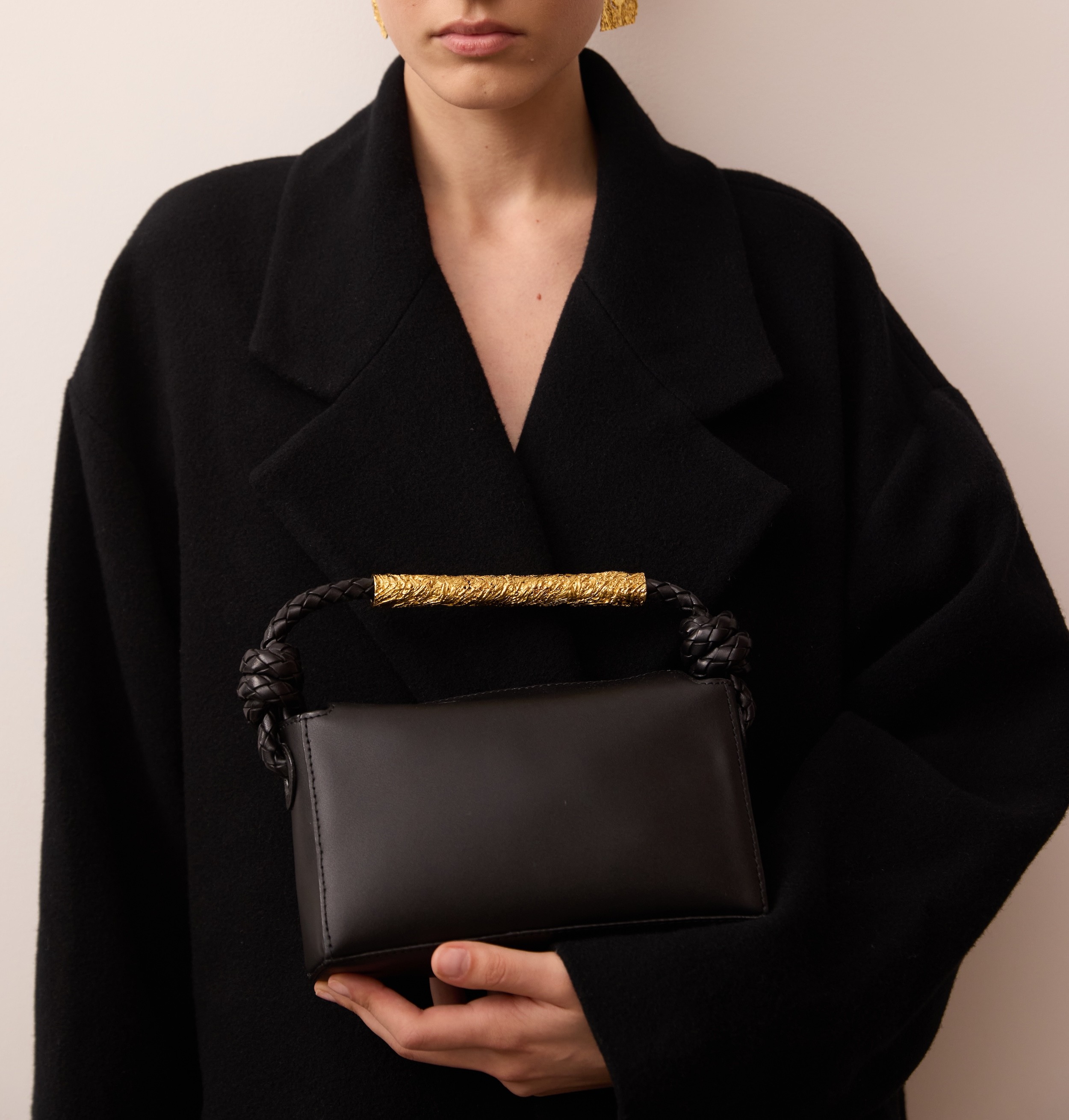 Woman in a light green long-sleeved dress holding a small cream-colored leather handbag with gold hardware in both hands.