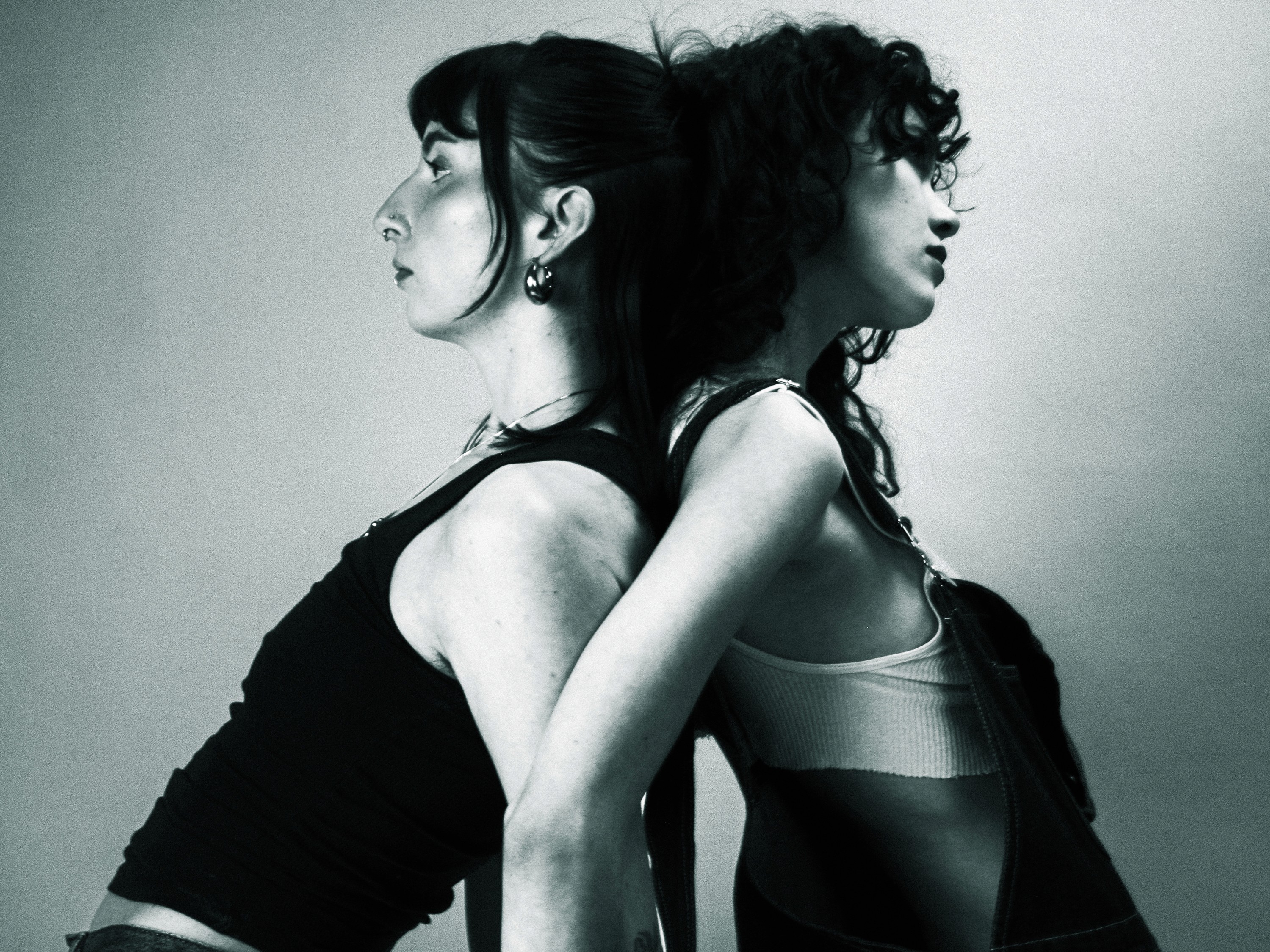 An image of two people leaning back-to-back against each other. The photo is stylized in black and white.