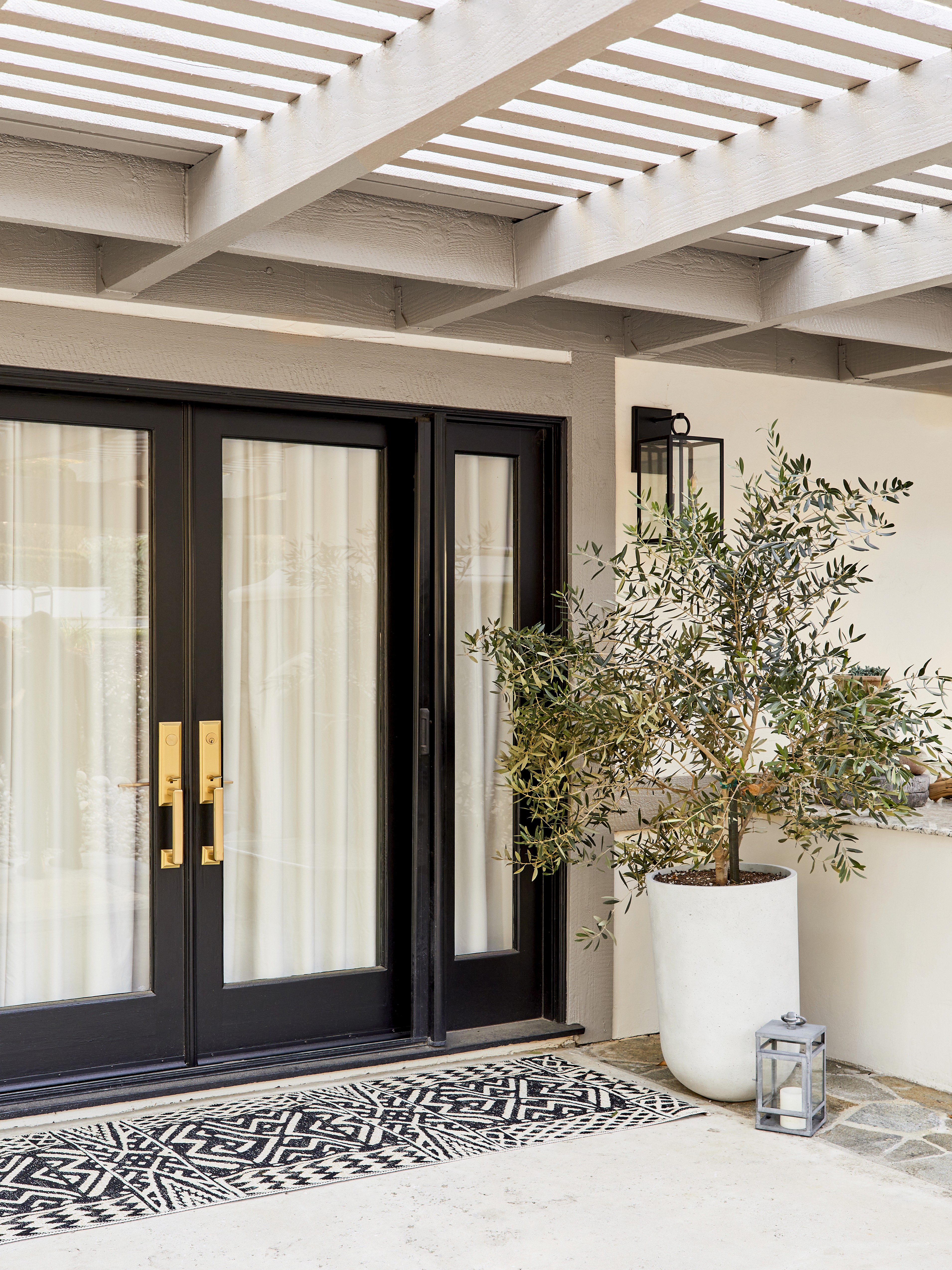This landscaped outdoor retreat blends East Coast charm with Southern California sunshine, featuring a cozy patio, an eight-person wooden dining table, and rattan light fixtures for a warm, inviting ambiance