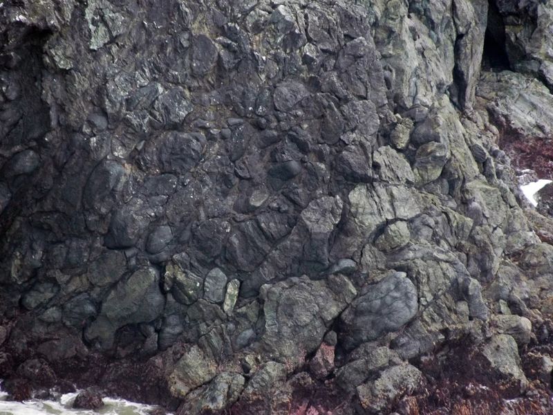 Close-up of pillow lava in Iceland, showing rounded, overlapping basalt formations formed by underwater eruptions, with smooth, bulbous textures stacked along a rocky shoreline.