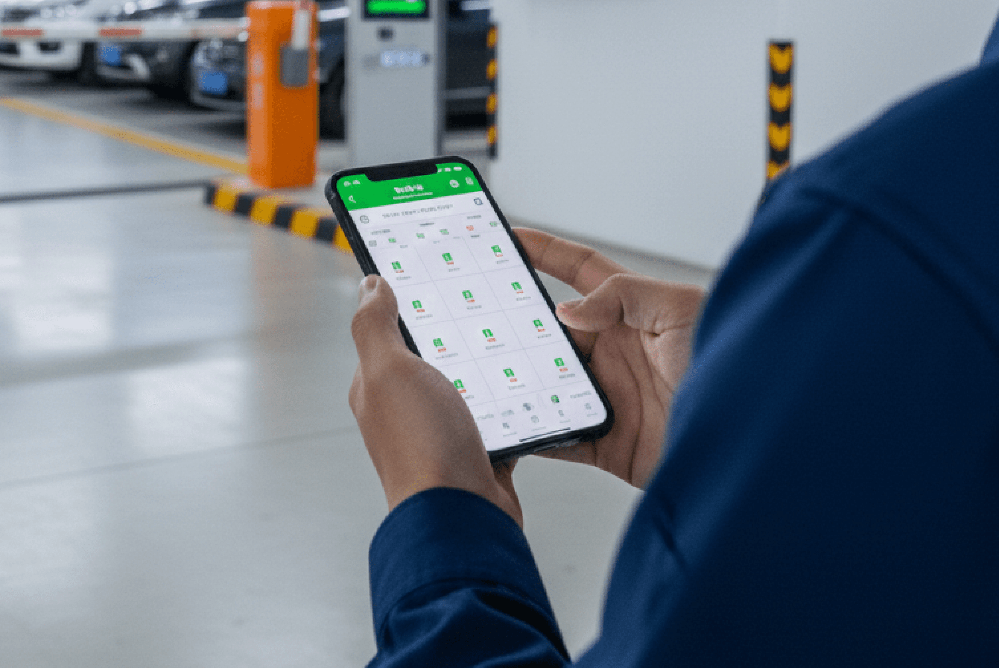 주차장 내부에서 남성이 스마트폰으로 녹색 UI의 주차 관제 앱을 사용하고 있으며, 배경에 차단기와 정산기가 설치된 주차 공간이 보입니다.