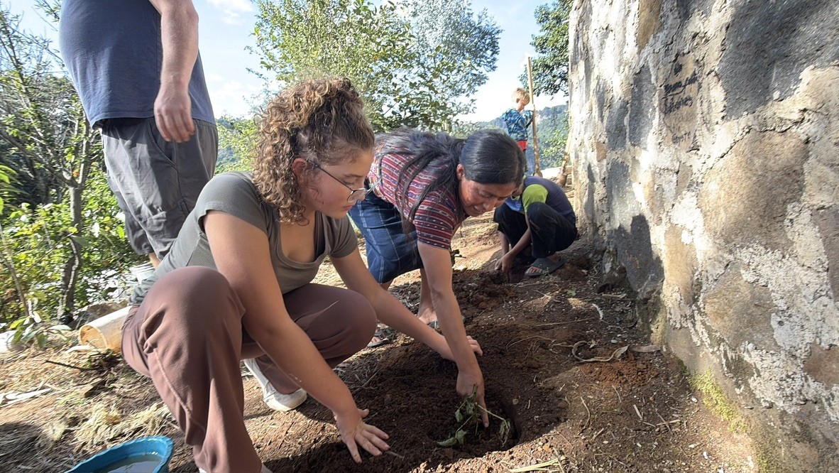 A young person and a woman planting beside a wall.
