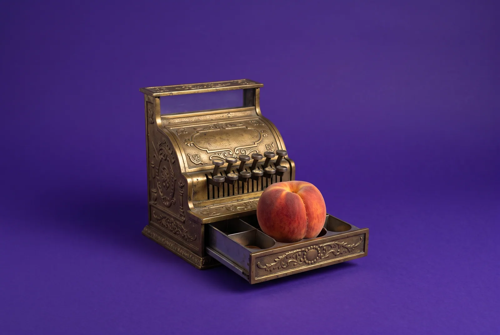 A peach sitting in the open drawer of a brass cash register, comparing prices of Fortify alternatives