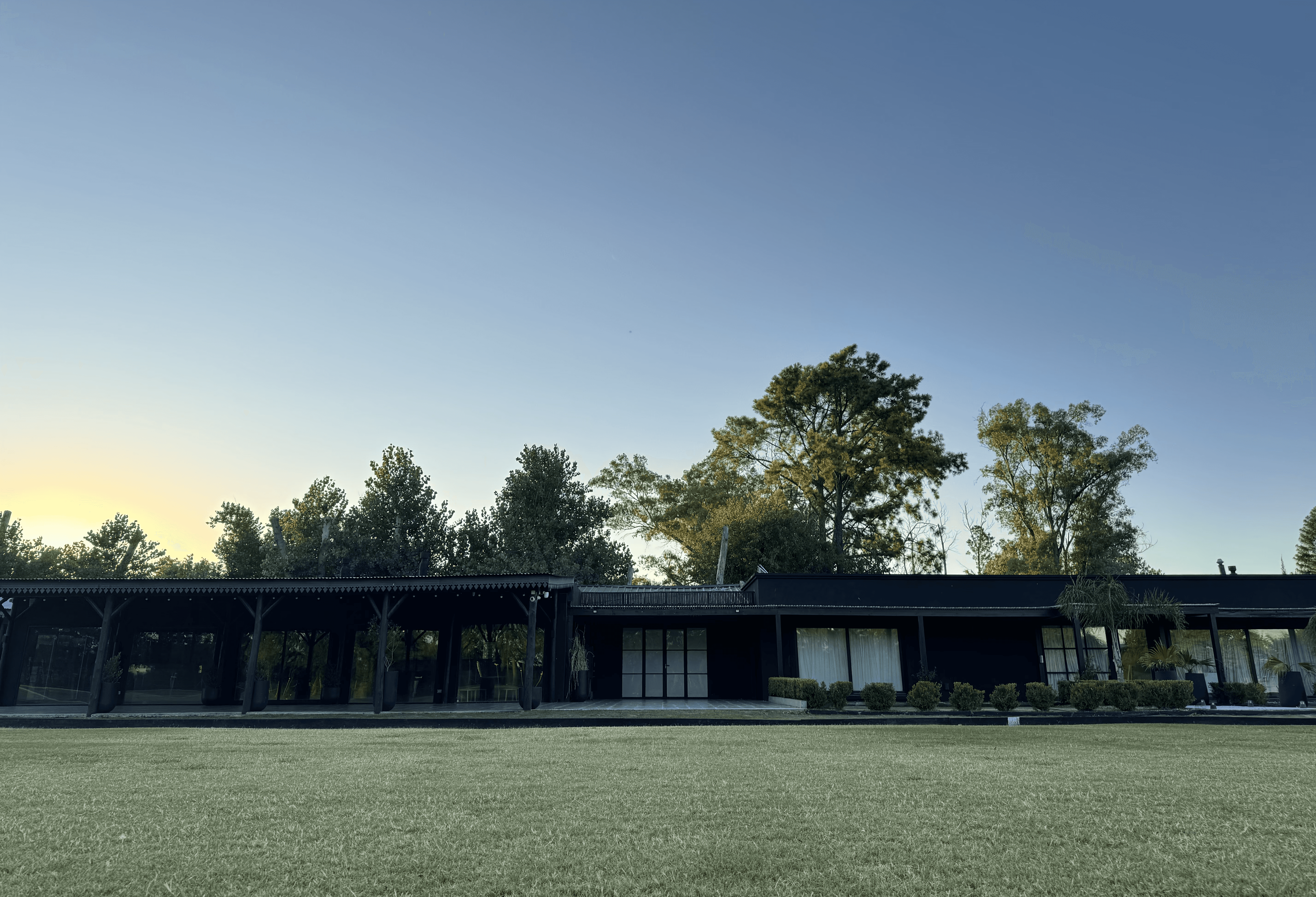 A young person with curly hair smiles at the camera while sitting in front of a laptop against a dark background.