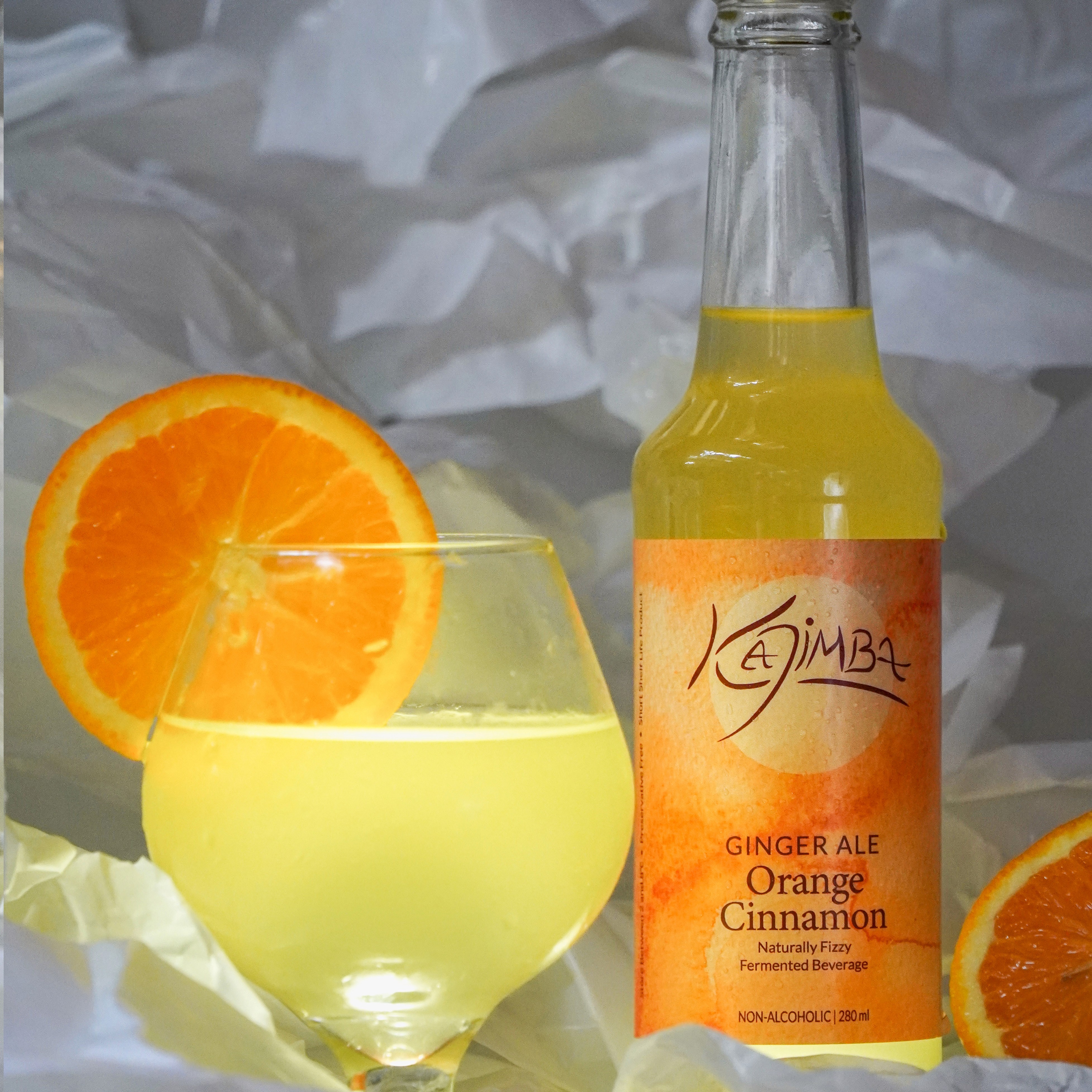 Orange Kajimba bottle next to a glass filled with Kajima and adorned by an orange slice.