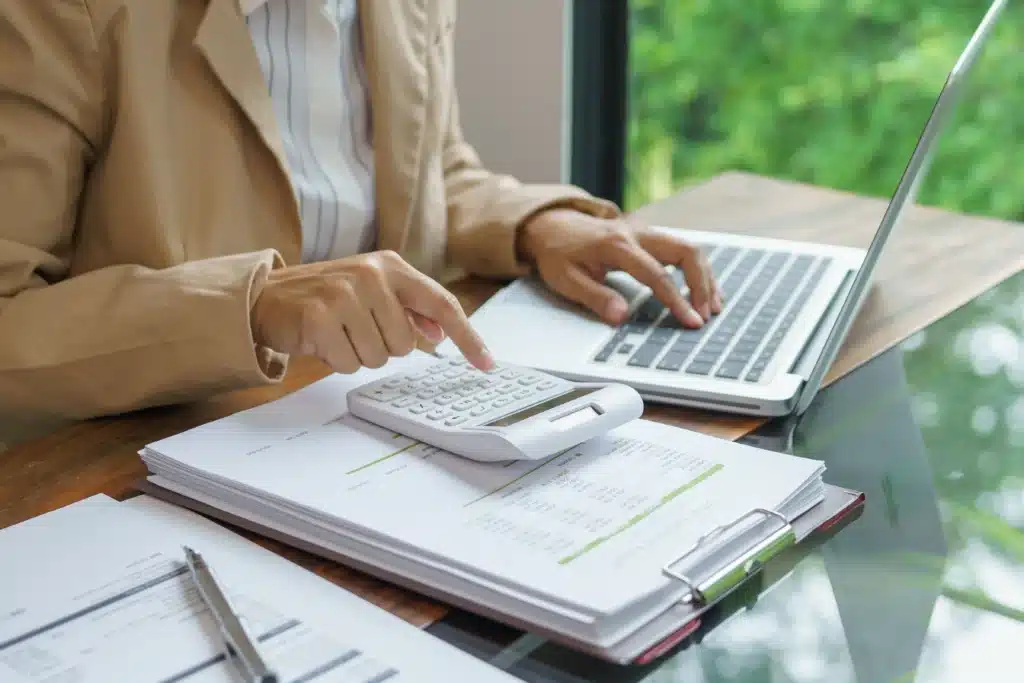 Best rental property management software landlord calculating expenses with calculator, paperwork, and laptop at office desk.