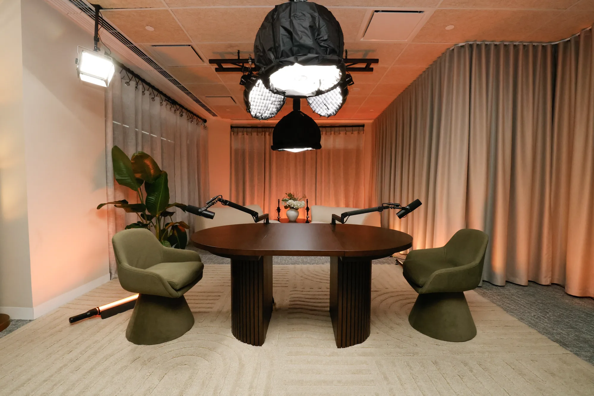 OAK set: a dark round table with green chairs and microphones in the cinema-grade room