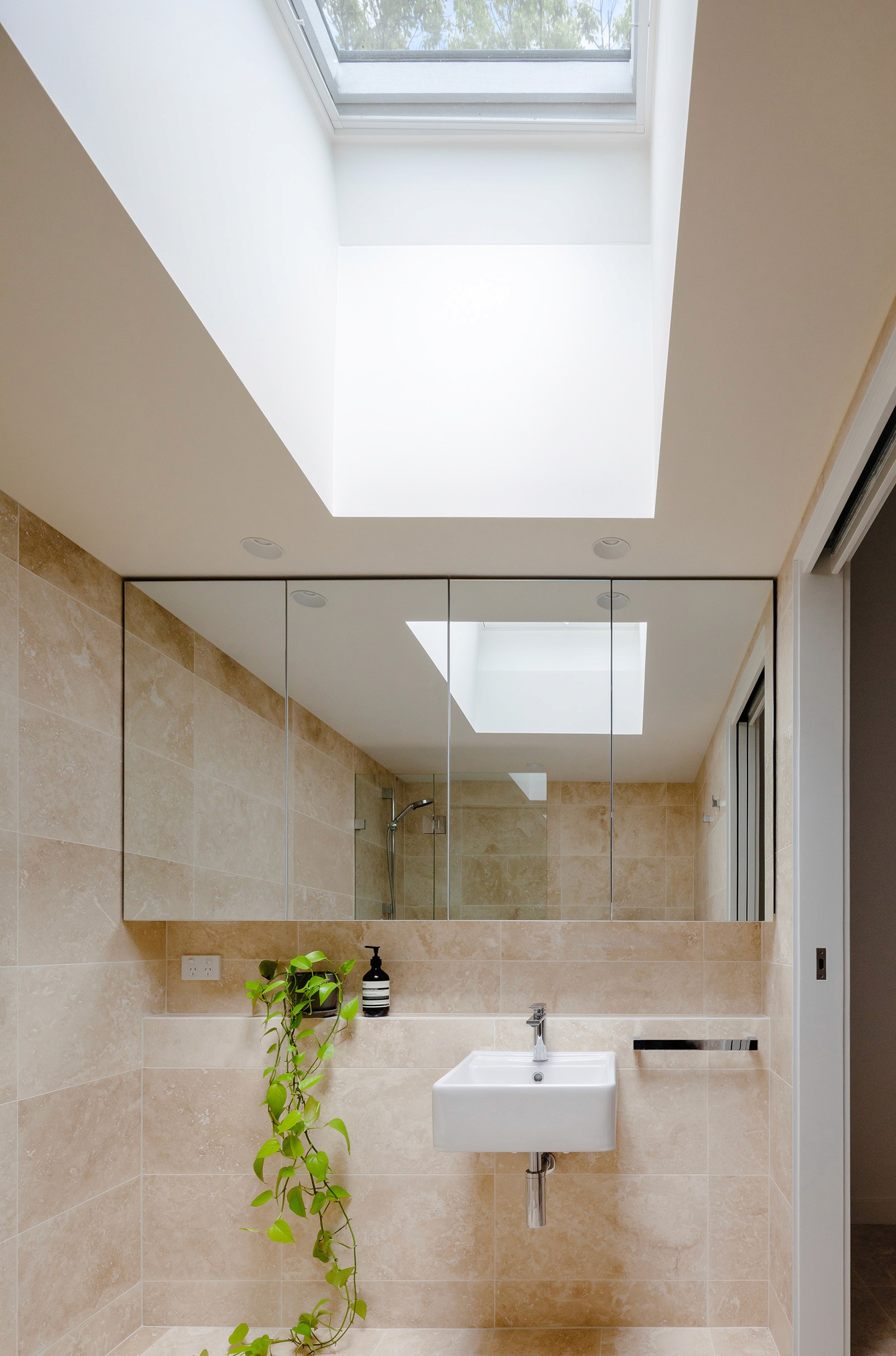Bathroom interior featuring travertine finishes, a skylight bringing daylight deep into the space, and a pared-back, functional layout.
