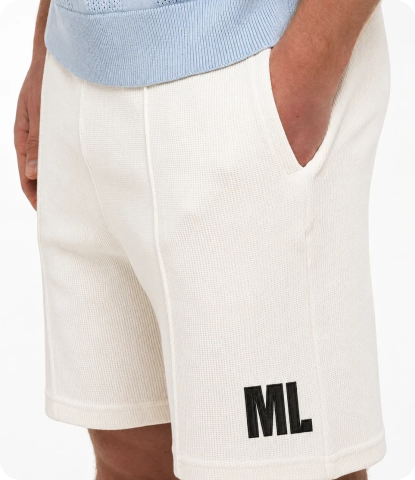 Cream waffle-knit shorts printed with the black block "ML" on the leg, worn with a pale blue knit top.