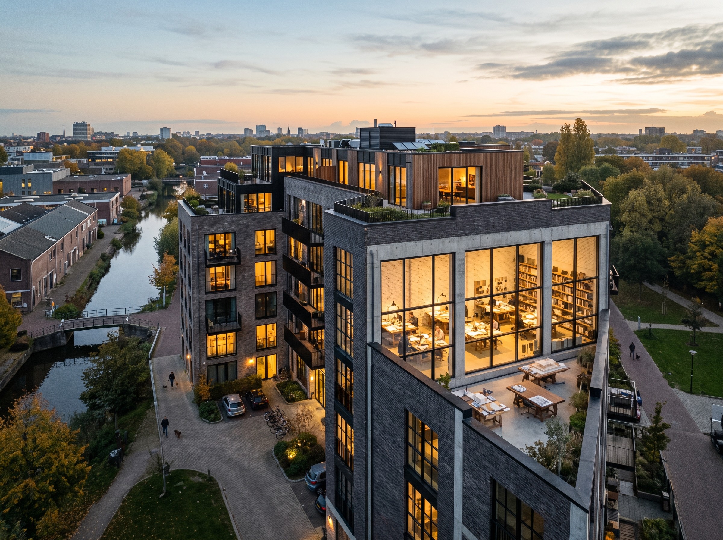 A modern, multi-story apartment building with large, illuminated windows showcasing a cozy interior, set beside a tranquil canal and surrounded by lush, green trees at sunset.