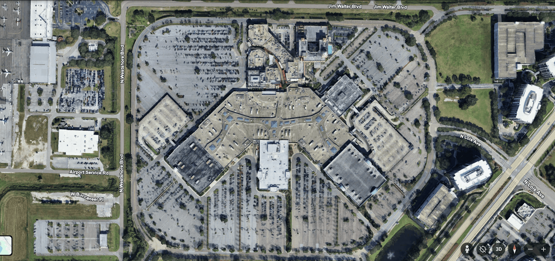 Aerial view of International Plaza shopping center showing the main mall building, extensive parking areas, surrounding roads, green spaces, and neighboring properties