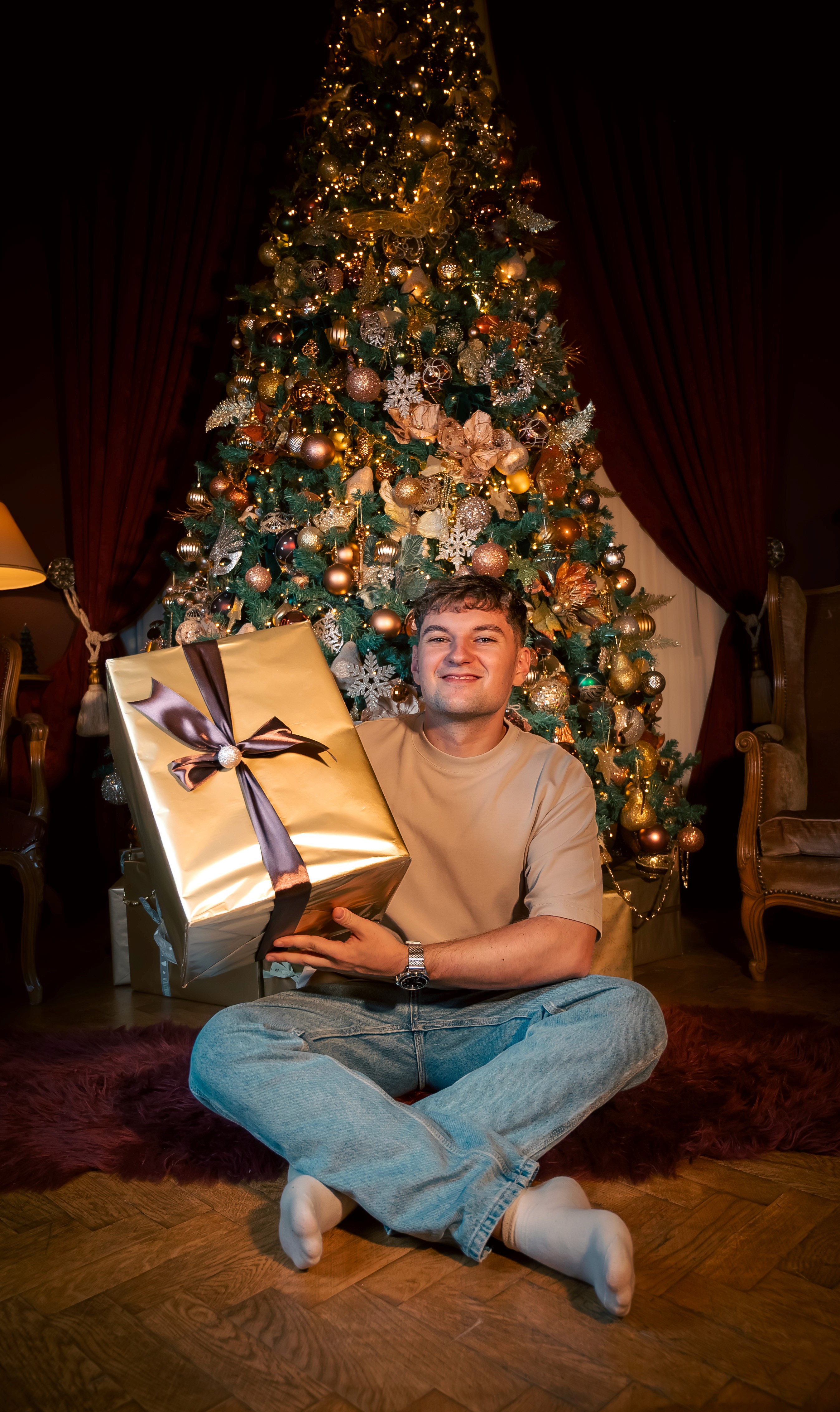 Portret de Crăciun cu cadou, realizat într-un decor festiv cu brad și lumini ambientale.