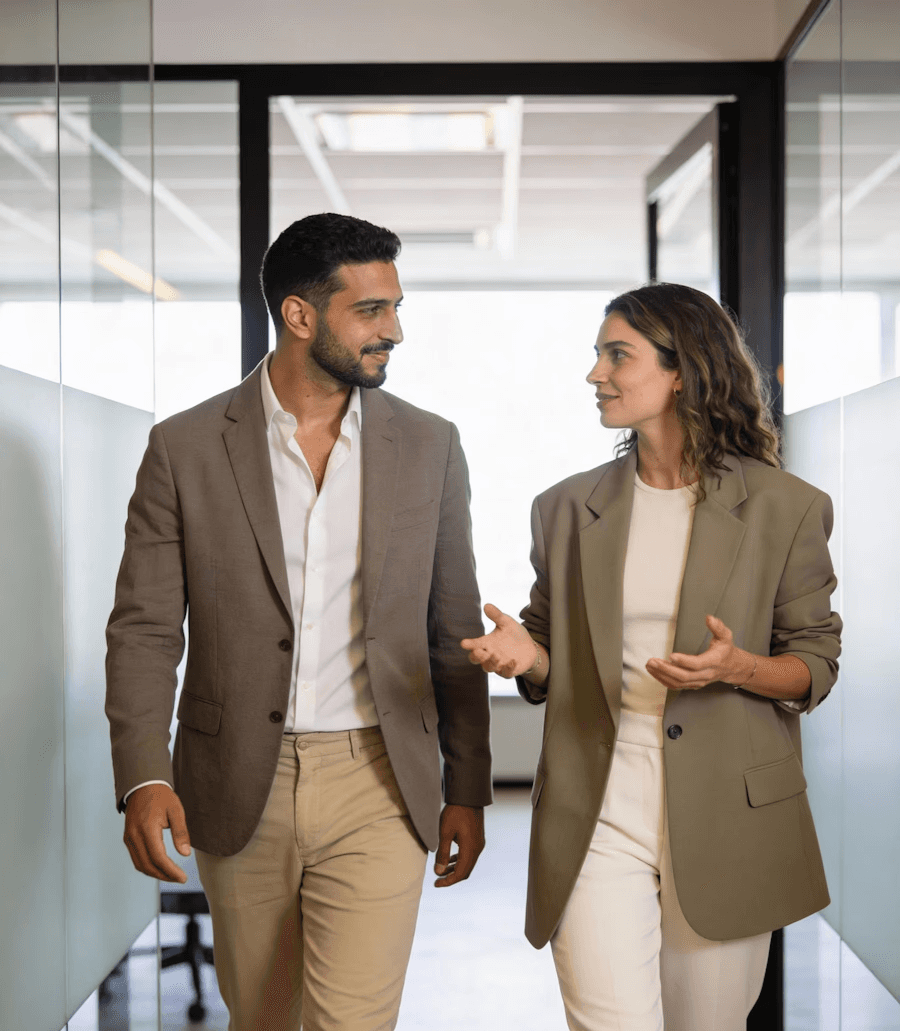 Two professionals walking and talking in an office hallway.