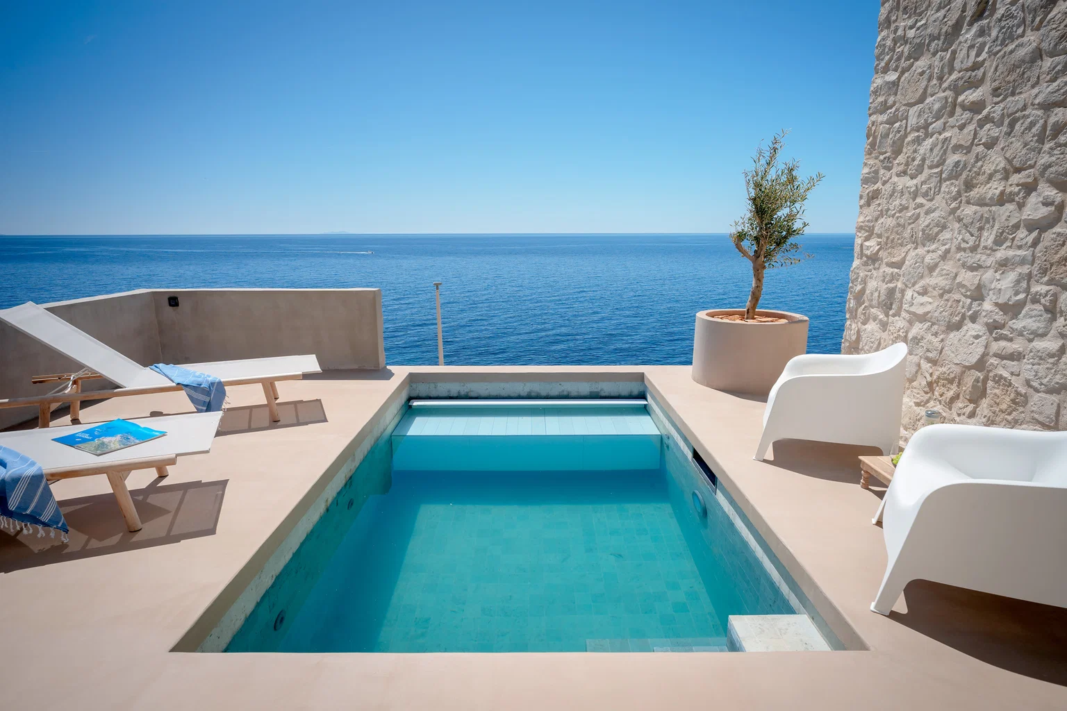 nfinity pool blending into the ocean view, minimalist sun loungers in soft neutral fabric, curved architecture