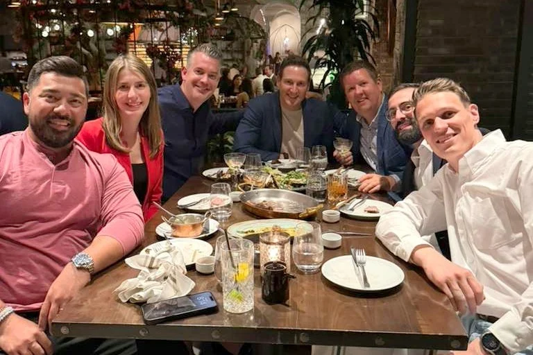 Group of colleagues gathered around a restaurant table with shared dishes and drinks.