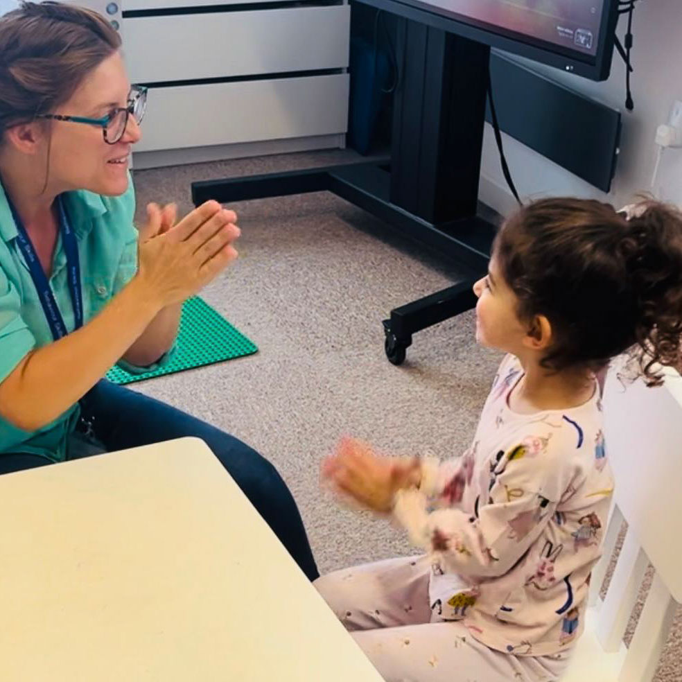 A facilitator is playing a game with a child. They're both sat at a small playing a hand clap game.desk