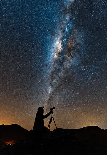 Observação astronômica no deserto do Atacama, com silhueta de pessoa fotografando a Via Láctea sob céu estrelado
