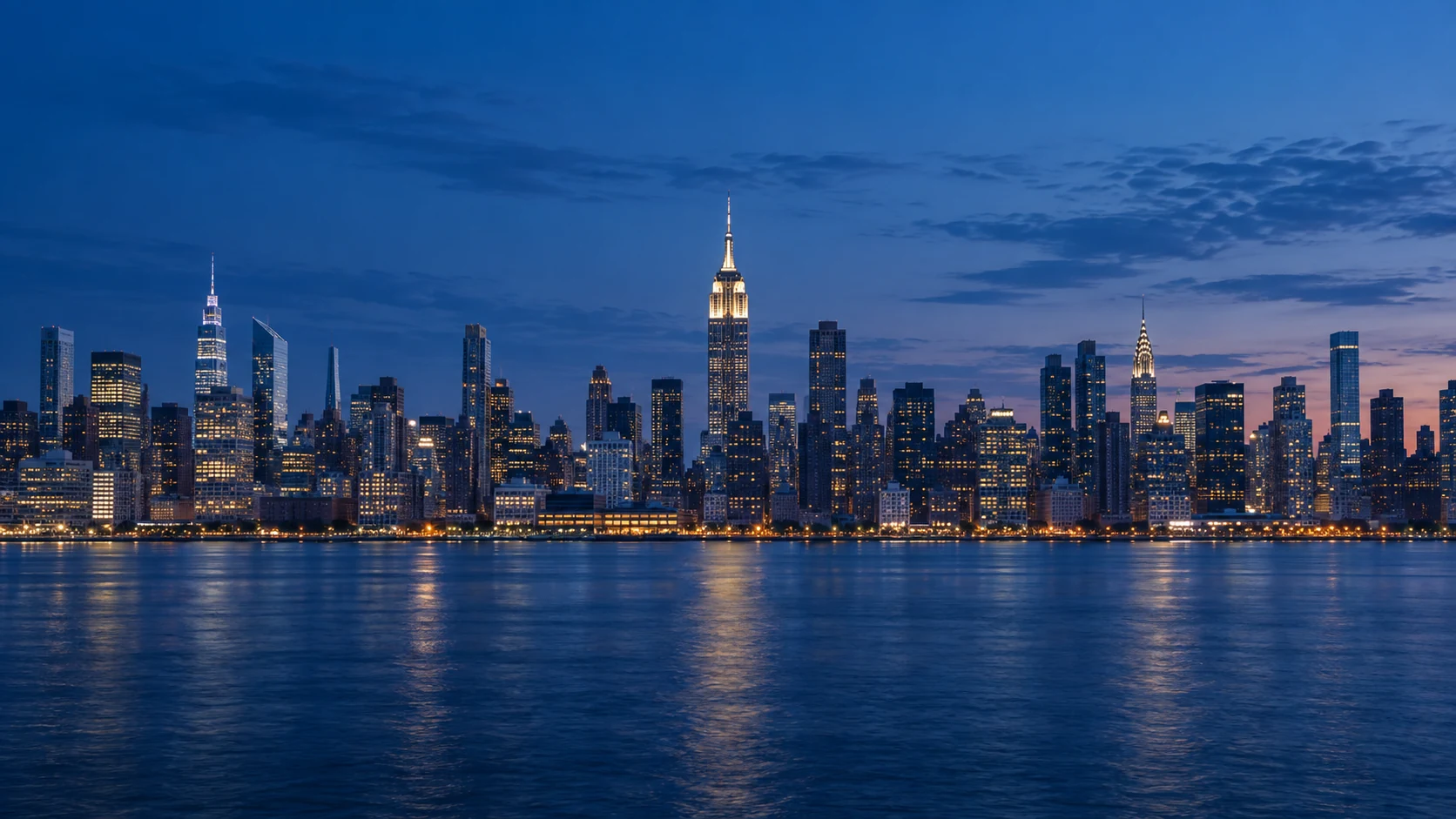 New York City skyline across the water at blue hour, centered on the Empire State Building.