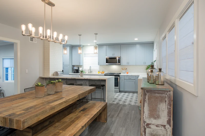 Alternate view of Rustic farmhouse dining room with kitchen in background. Grey floors and blue cabinetry. Photo by Chris Darnall.