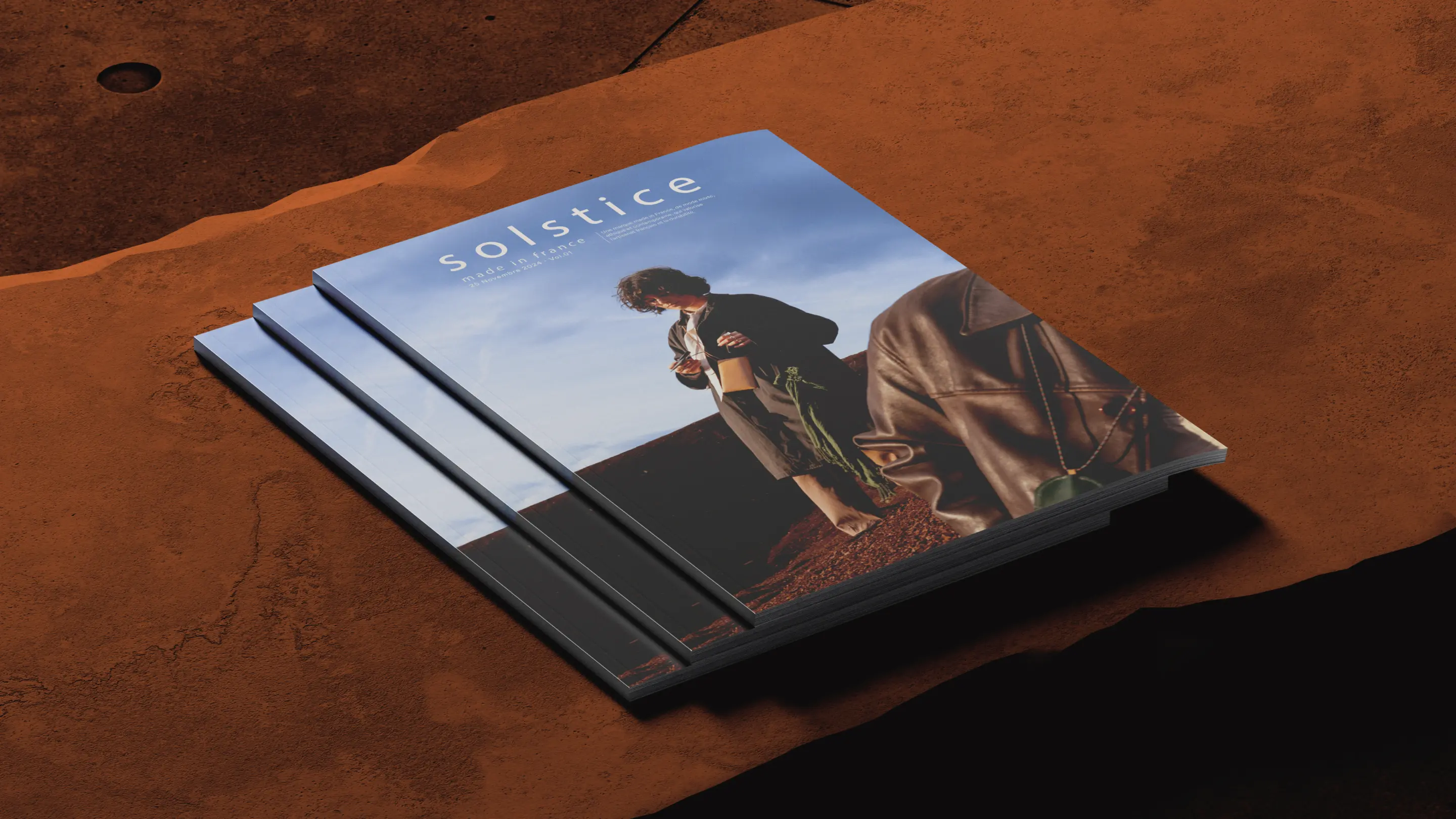 Three stacked Solstice magazines on a rust-brown surface, featuring a campaign image set in a mineral landscape on the cover.