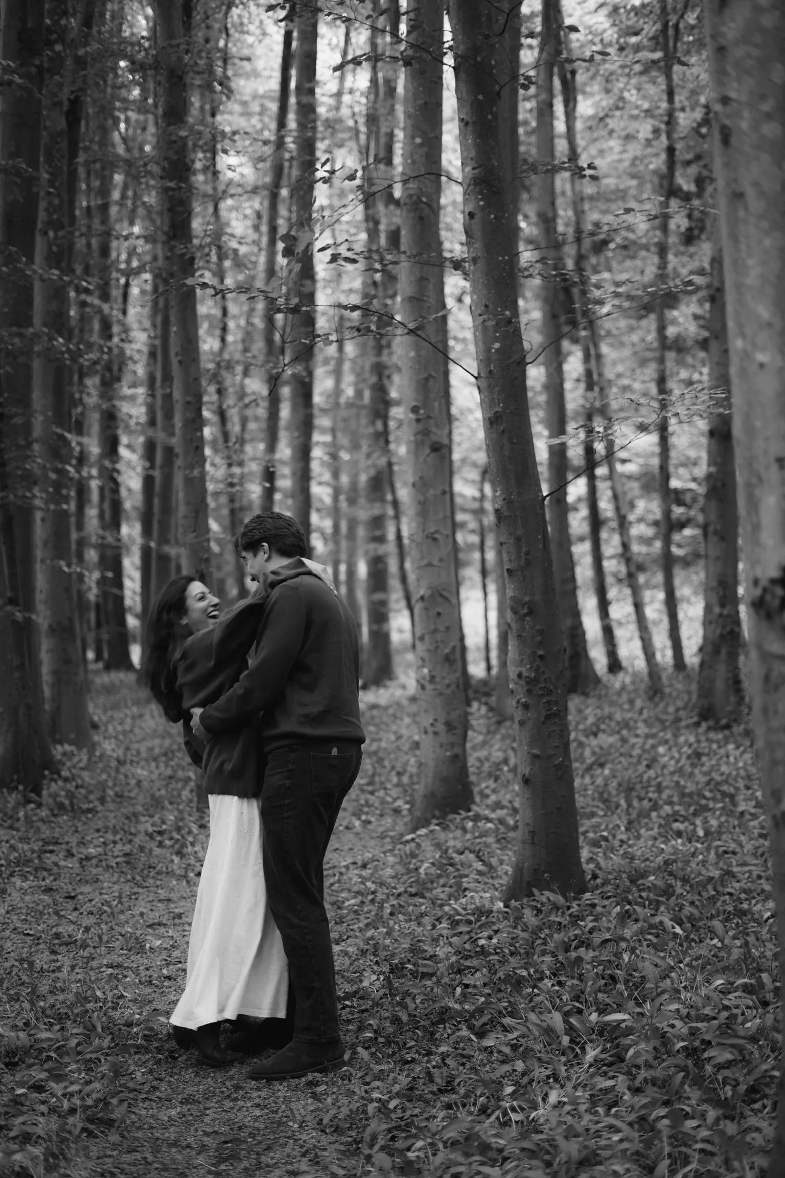 Connor and Cherine sharing a kiss in a black-and-white woodland portrait