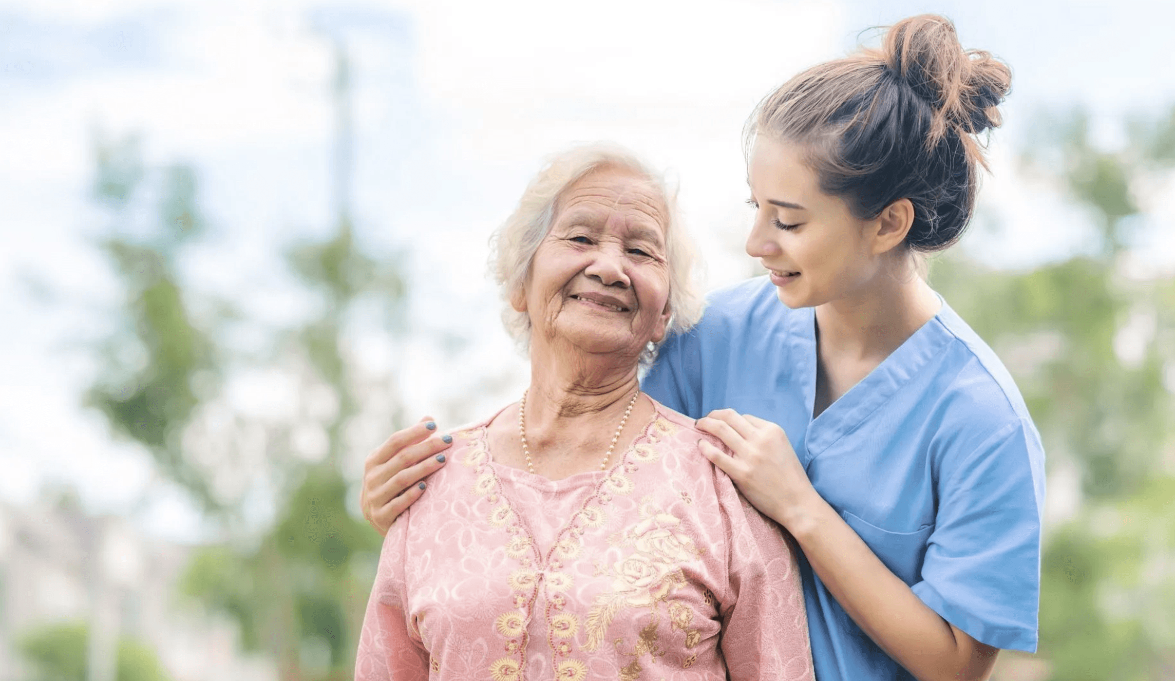 Smiling caregiver with an elderly woman outdoors in a sunny setting