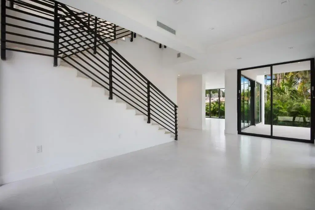 Modern interior staircase with black steel railing and open living area in Miami Beach home by Atelier International LLC