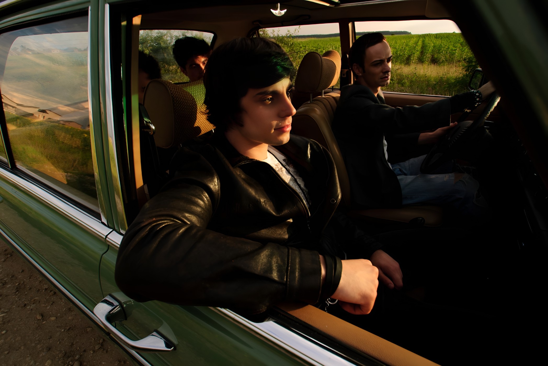 Members of Plastik Charm sitting inside a vintage green car at sunset, with the driver focused and others relaxed in the back seat.
