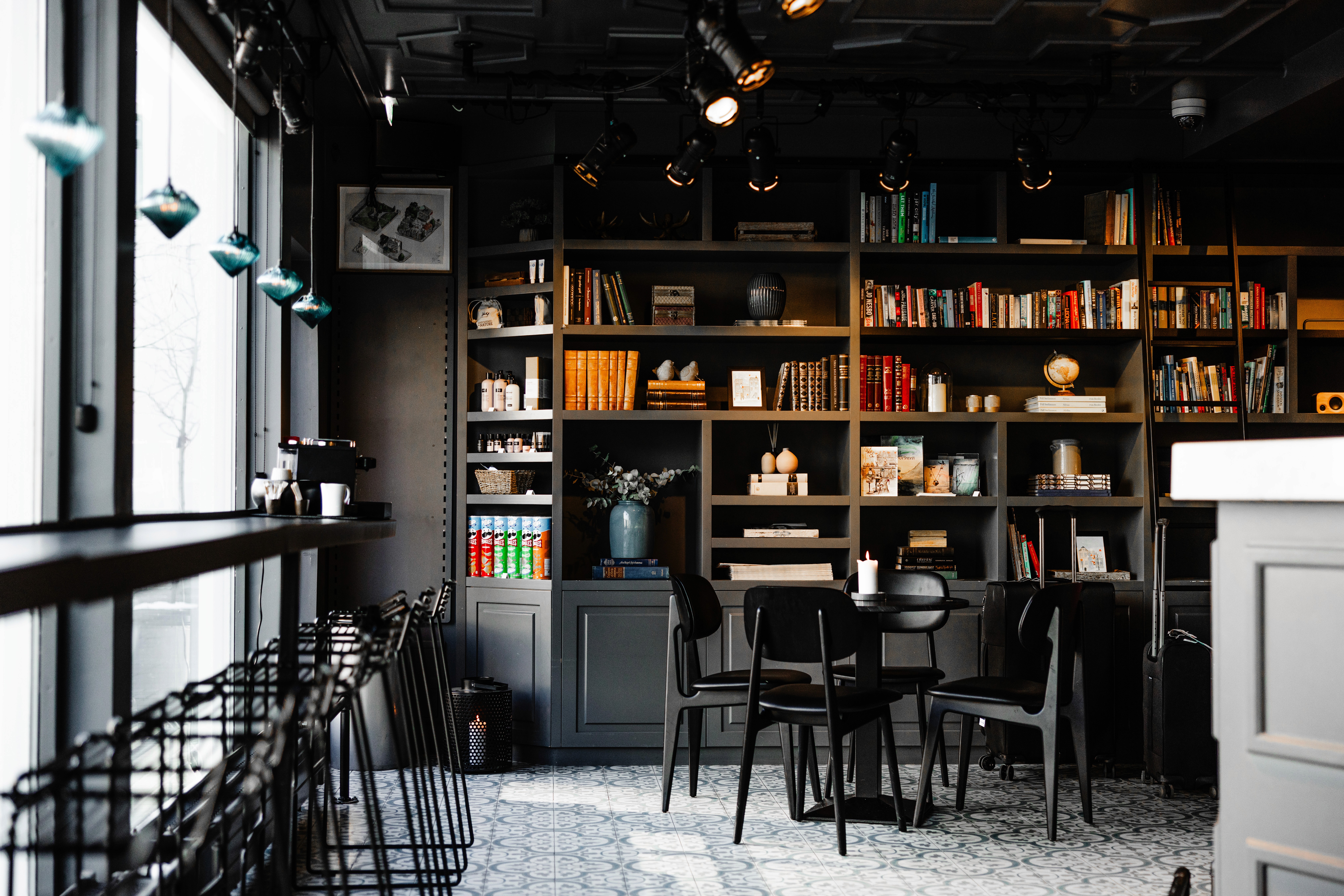 A stylish lounge in downtown Reykjavik has dark shelves, books, black chairs, and soft lights above the tables.