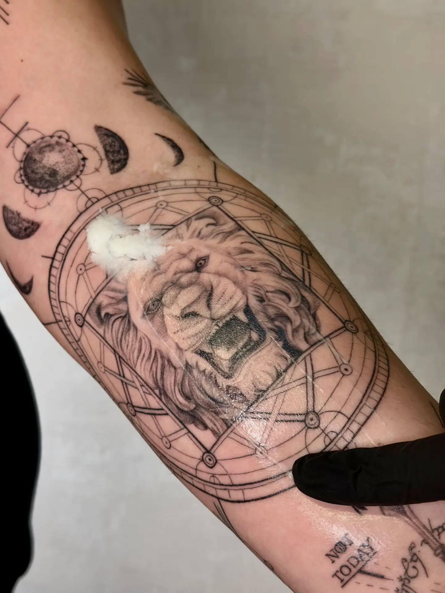 Healed micro-realism lion tattoo with intricate geometric framing, fine-line moon phases, and sword detail, showcasing high-contrast shading and technical mastery.