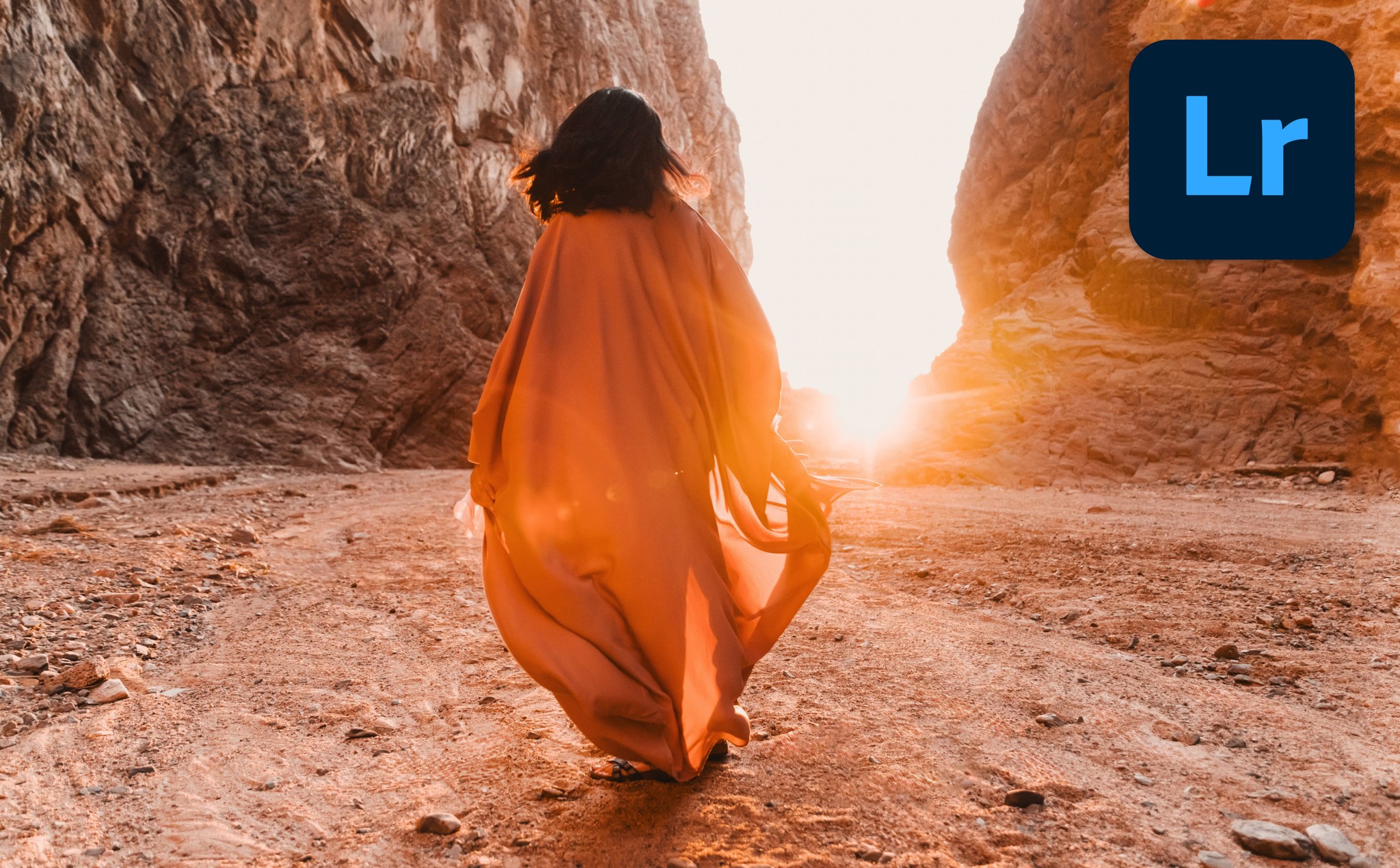 A person wearing orange looking toward the sun through two rocky hills