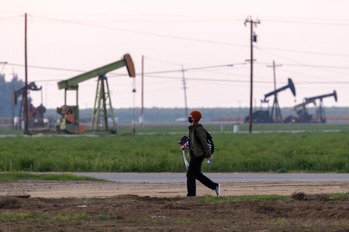 A man walking through farmland with oil rigs in the background.