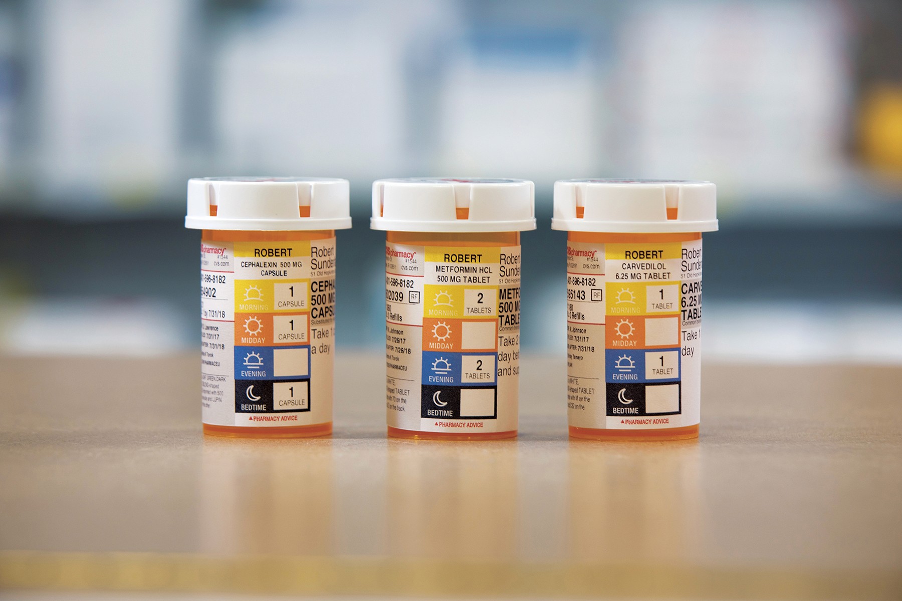 A photo of three identical pill bottles, each with a label depicting four colors and icons. Each color and icon represents a part of a day and on the other side how many pills must be taken. There is yellow with a sun representing morning, orange with the sun representing evening, blue with half of sun representing afternoon and black with a moon representing midnight.
