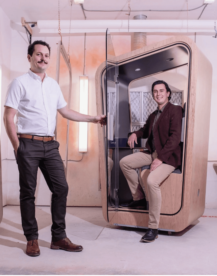 Two men pose with a Loop Solo Office pod in industrial looking space