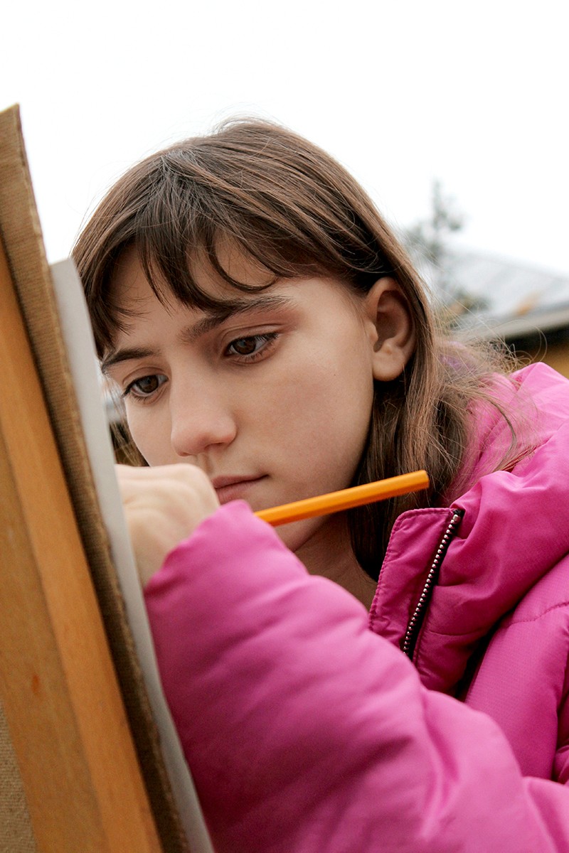 a girl in a pink jacket is holding a pencil