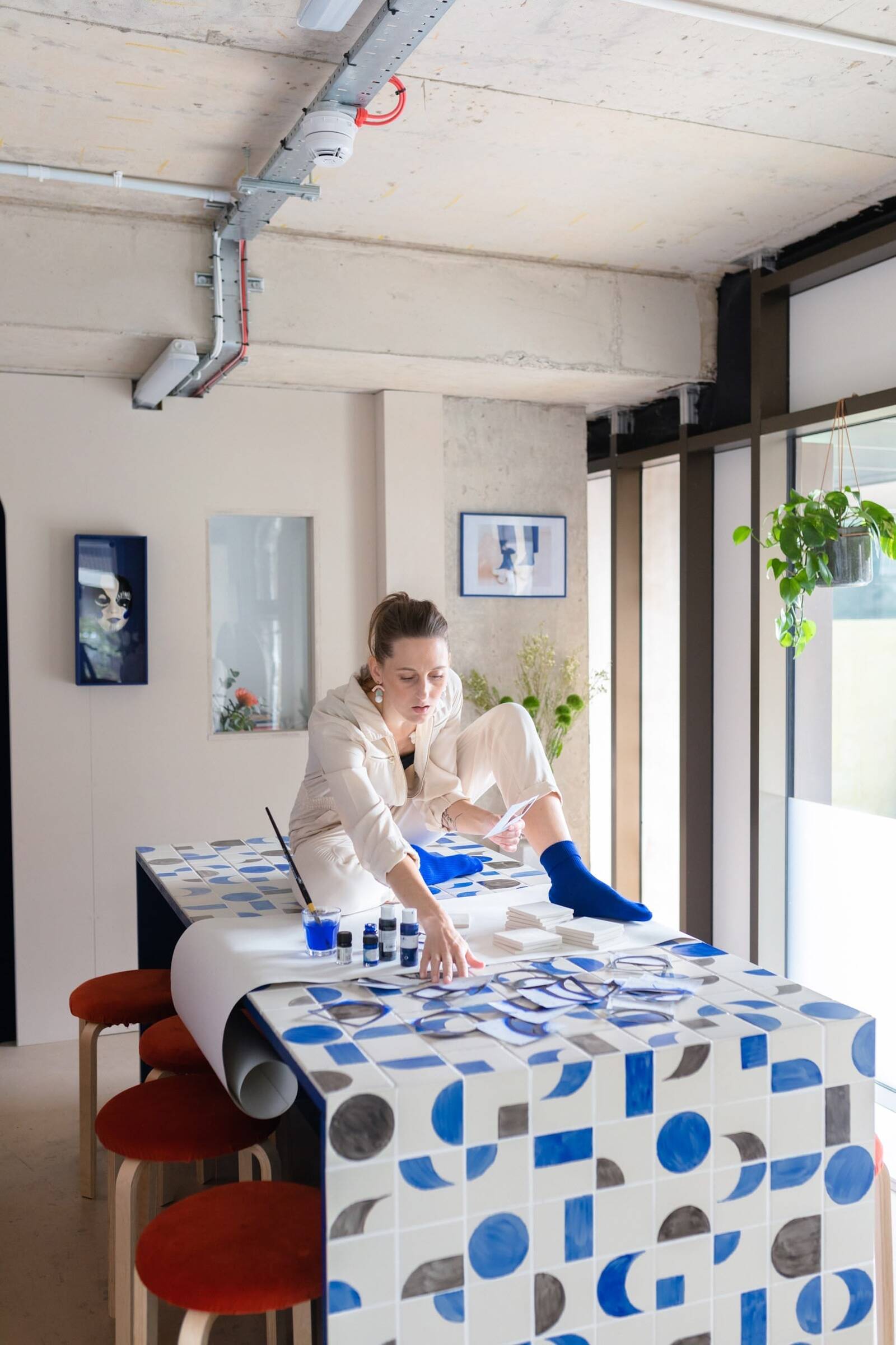 Judith, Sussex-based interior designer, with bespoke hand-painted tile centrepiece table in a playful studio setting