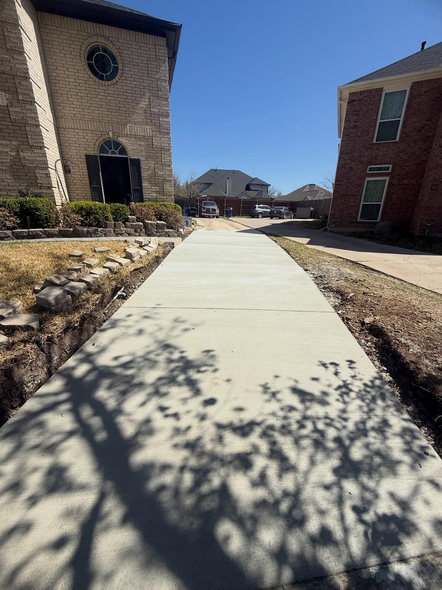 Newly completed concrete driveway extension running between residential homes, built by professional driveway contractors in Dallas.
